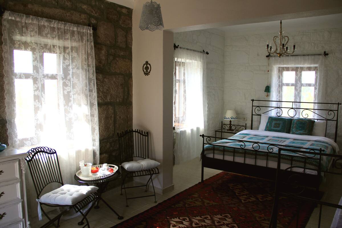 A bedroom with a bed, a chair, a table, and a chandelier.