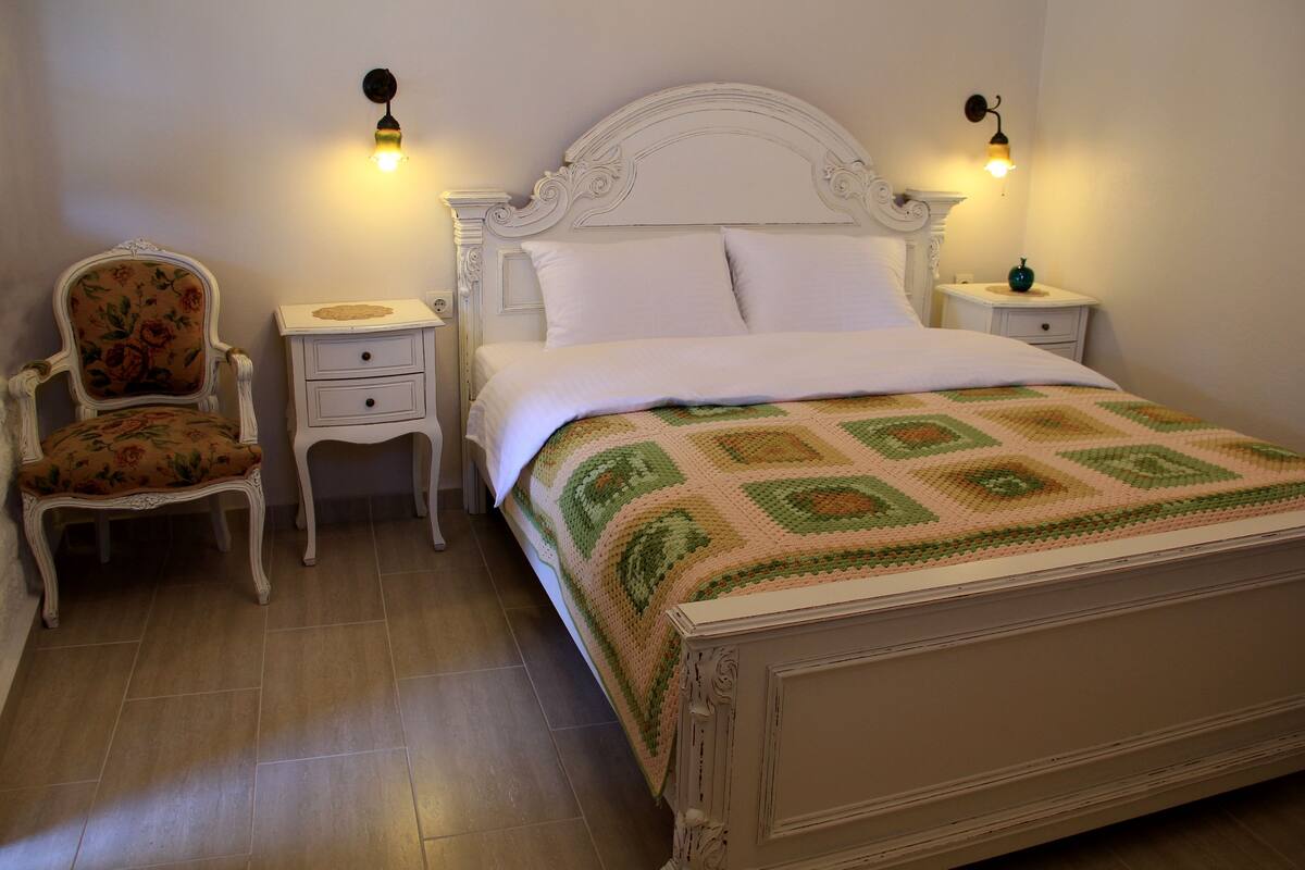 A bedroom with a bed, a chair, two nightstands, and wall-mounted lights.
