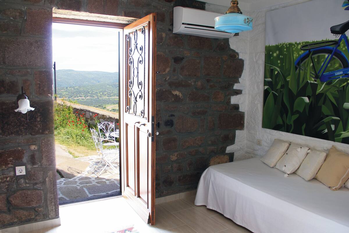 A bedroom with a stone wall, a bed with white bedding, and a view of the outdoors.