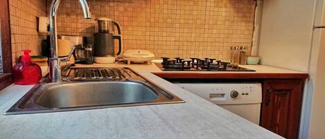 Una cocina con un lavaplatos de acero inoxidable, una estufa a gas, una cafetera y un lavavajillas.