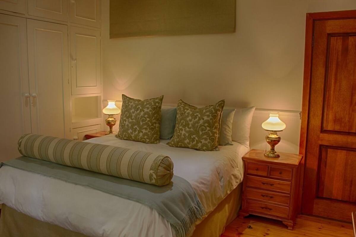Een slaapkamer met een bed, twee nachtkastjes met lampen, een houten garderobe en een deur.