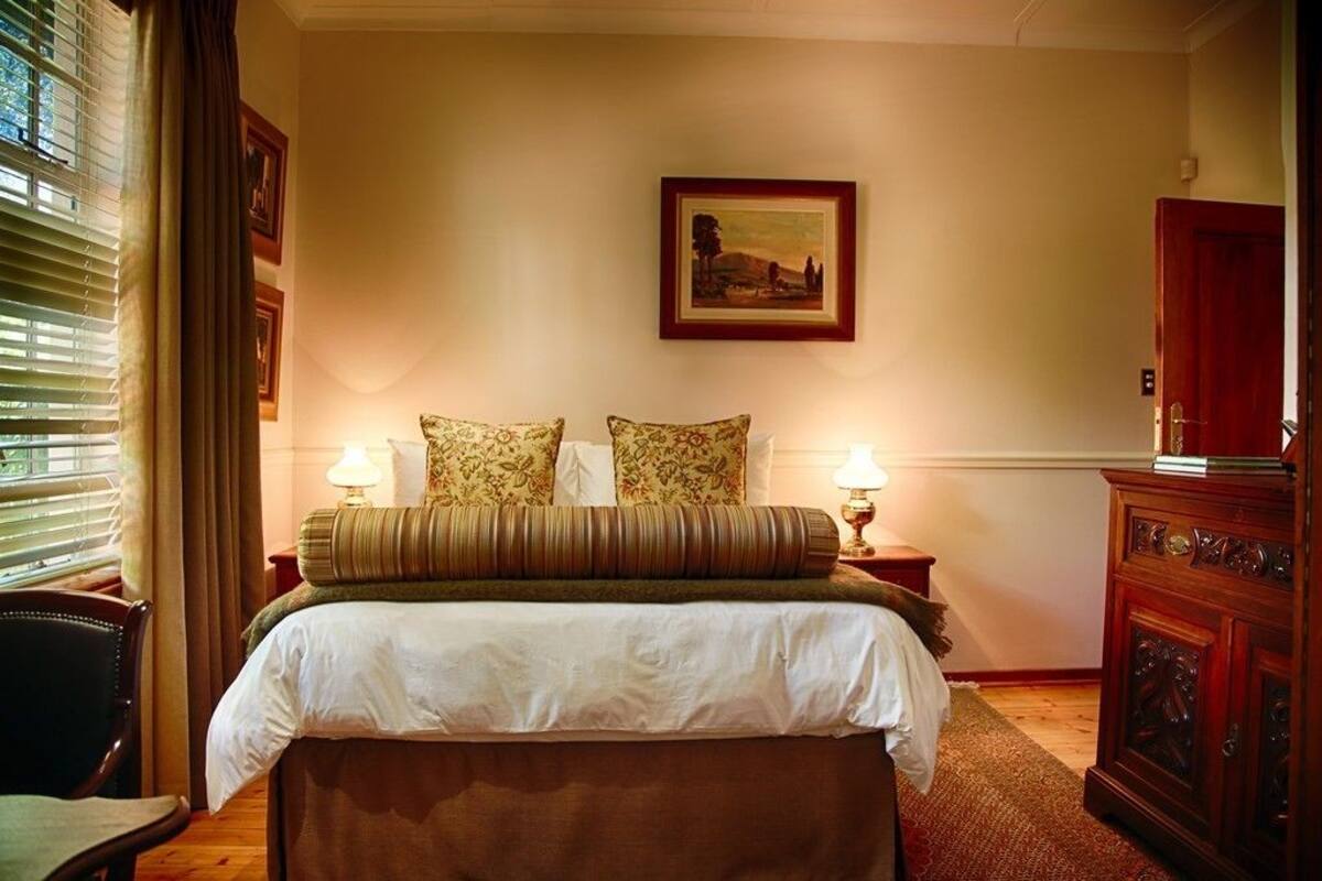 Een keurig opgemaakte slaapkamer met een groot bed, twee bedlampjes, een ingelijst schilderij aan de muur en een houten kast.