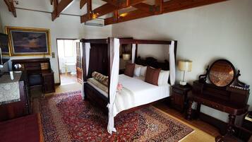 A four-poster bed with a canopy, a large ornate mirror, and a red patterned rug in a room with wooden beams and a large painting on the wall.