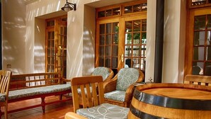 A cozy seating area with a wooden bench, two wicker chairs with patterned cushions, and a round wooden table. - Kleine Constantia (Roodepoort)
