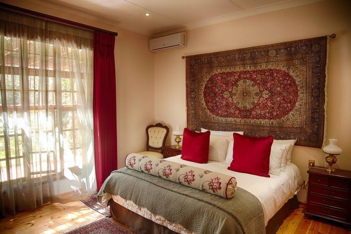 Een slaapkamer met een groot bed, een decoratief wandtapijt, een houten hoofdeinde, een nachtkastje en een raam met dunne gordijnen.