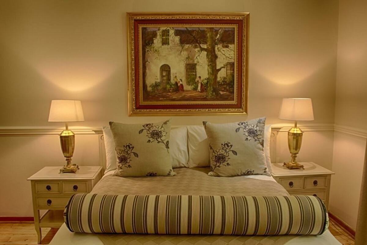 Een keurig opgemaakt slaapkamer met een bed, twee nachtkastjes, twee lampen en een lijst met een schilderij aan de muur.