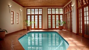 An indoor swimming pool with wooden beams, large windows, and potted plants. - Kleine Constantia (Roodepoort)