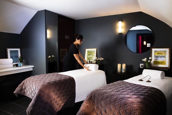 Habitación de hotel con dos camas, un espejo, tocador con artículos de aseo y diplomas enmarcados en la pared.