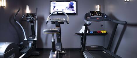 A gym with a treadmill, elliptical, and stationary bike, a TV on the wall, and a shelf with exercise balls.