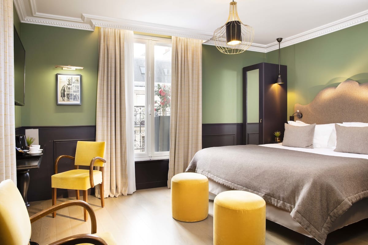 Un dormitorio con cama, una silla, una mesita y una ventana con cortinas.