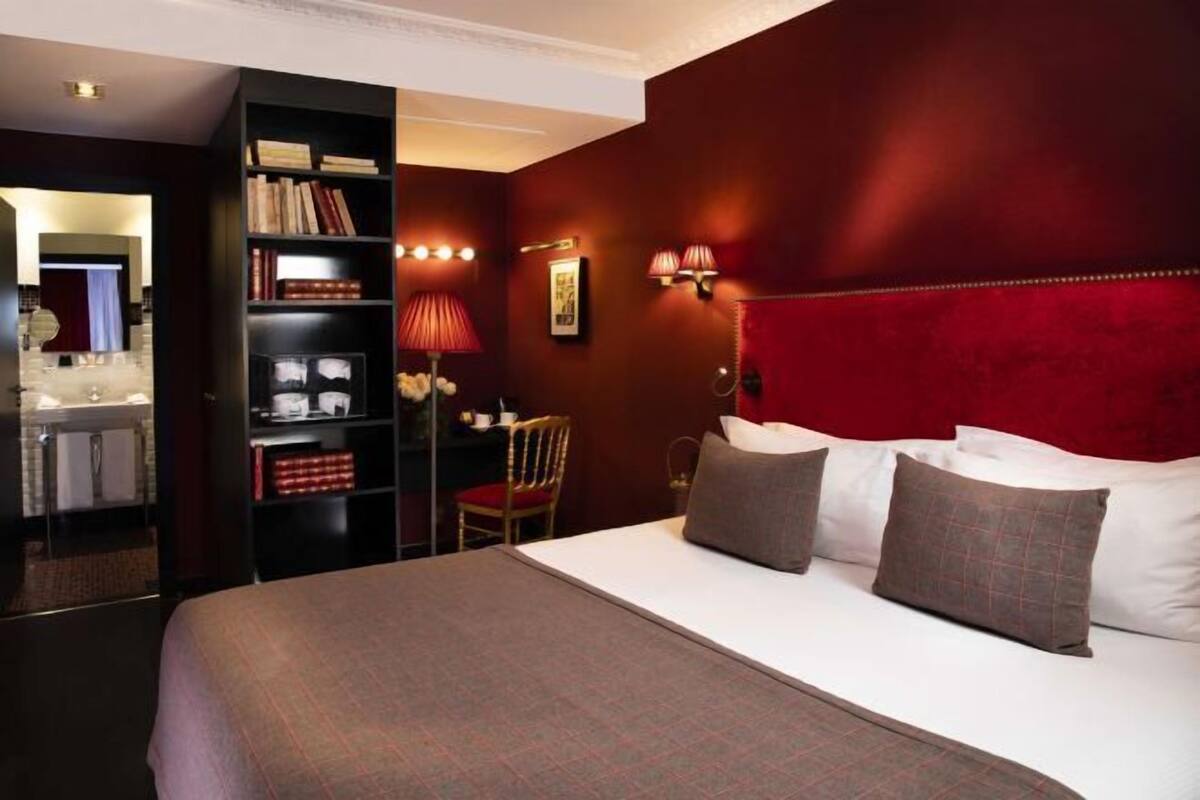 Habitación de hotel con una cama grande, una estantería, un escritorio y una pared de acento roja.