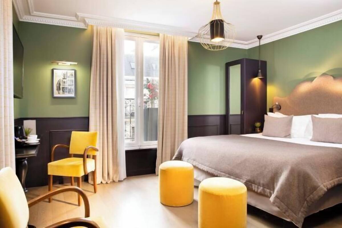 Habitación de hotel con cama, una silla, un escritorio y una ventana con cortinas.