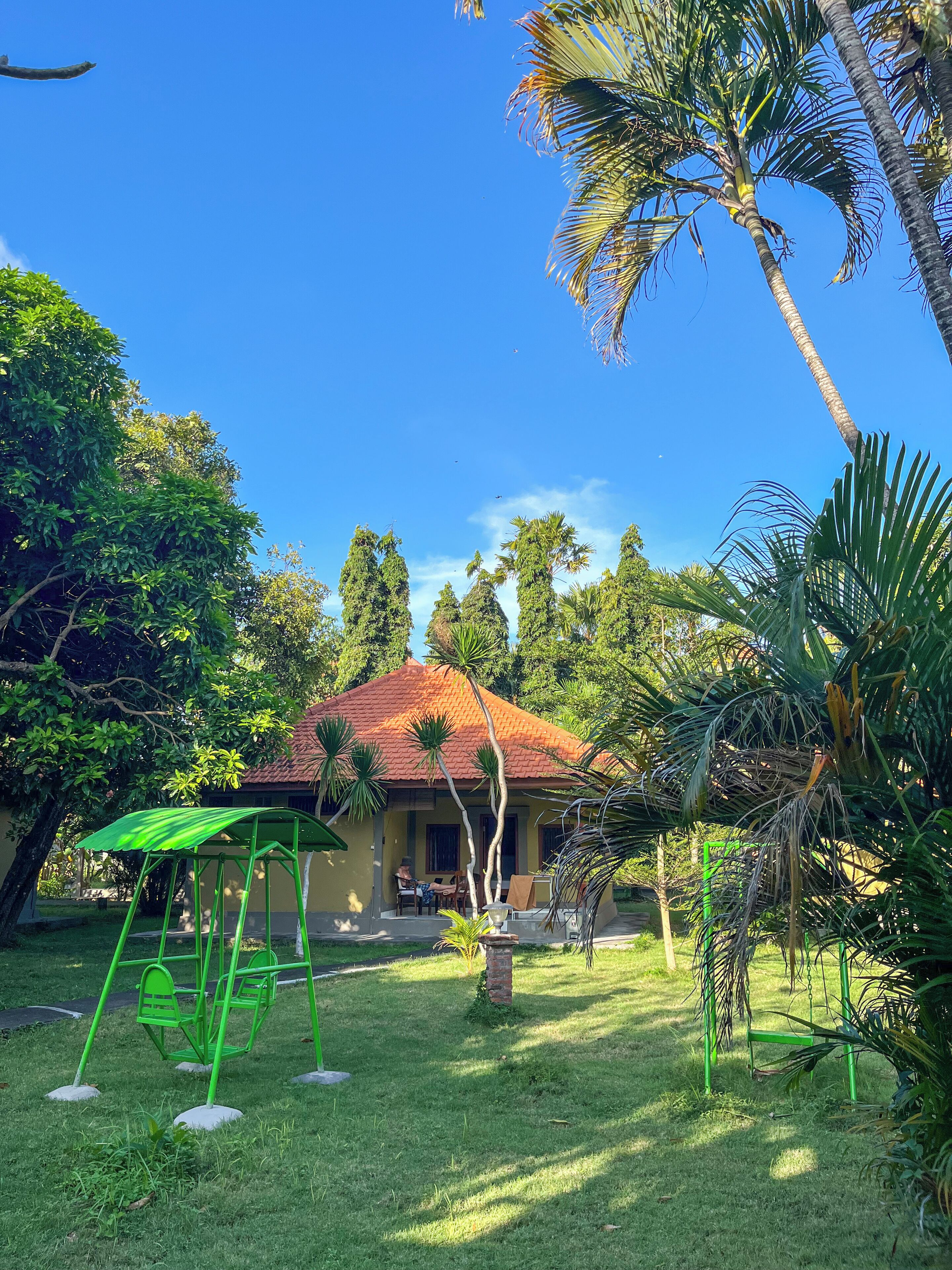 A house with a red roof, surrounded by lush greenery and palm trees.
