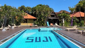 A clear blue swimming pool with the word "SUJIS" painted on the water, surrounded by lounge chairs and palm trees. - Suji Bungalow (Kuta)