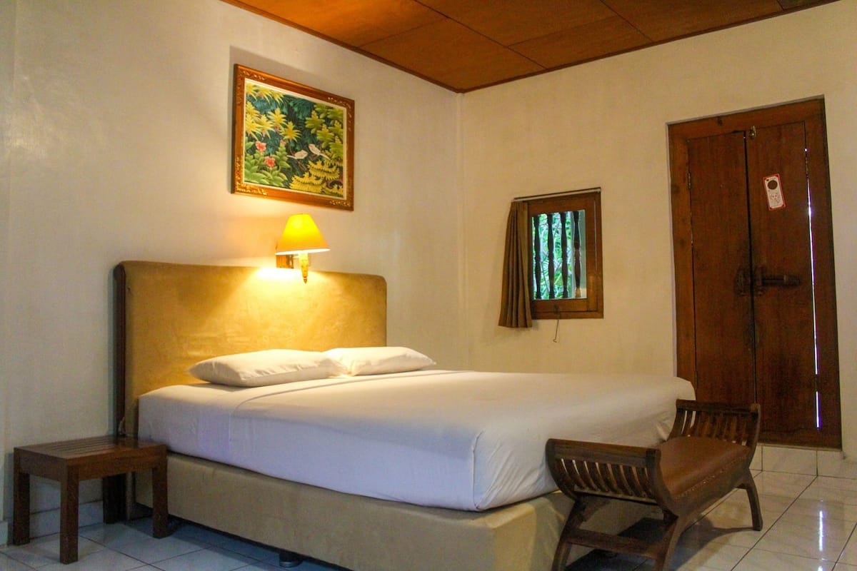 A hotel room with a bed, a nightstand, a chair, a wooden door, and a window with curtains.