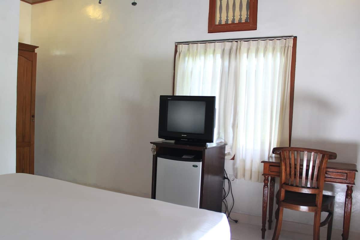 A hotel room with a bed, a television on a stand, a small refrigerator, a wooden chair, and a window with curtains.