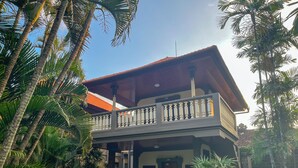 A two-story building with a balcony, surrounded by palm trees. - Suji Bungalow (Kuta)
