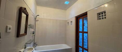 A bathroom with a bathtub, a sink, a mirror, and a window with a view.