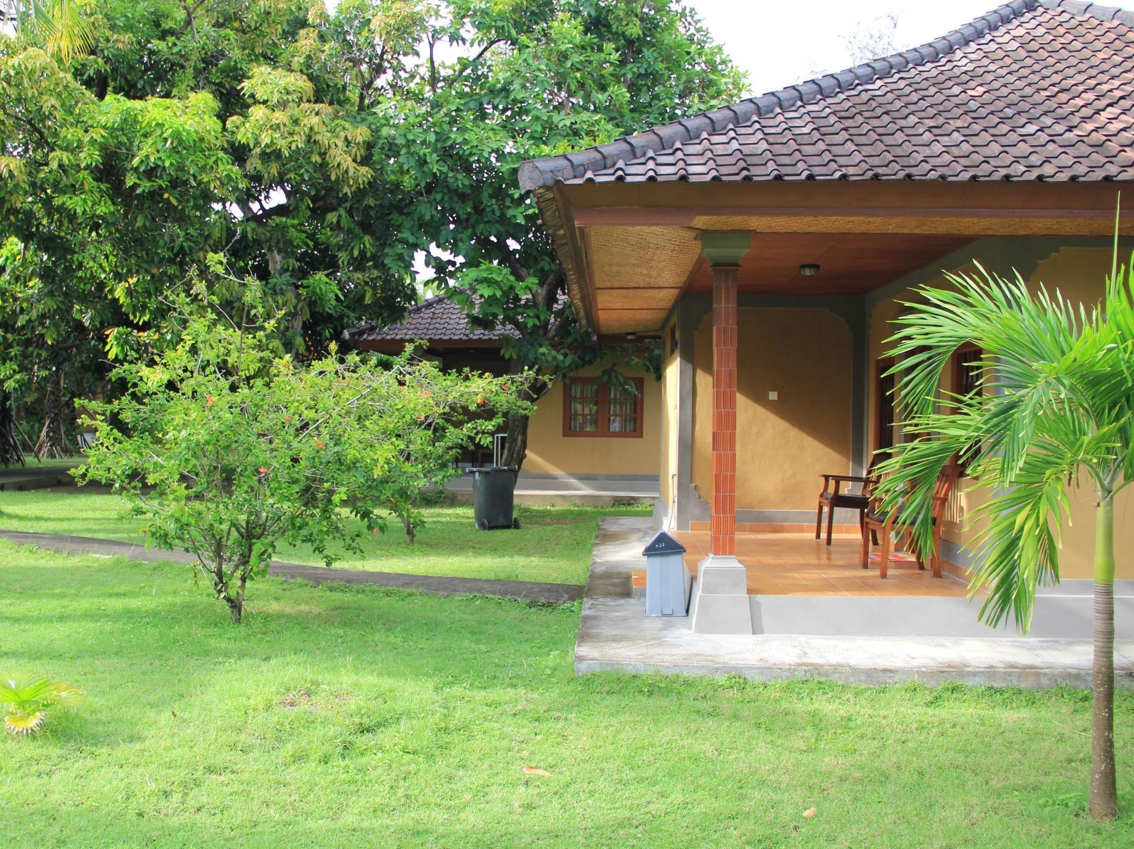 A house with a tiled roof, a porch with chairs, and a small lawn.