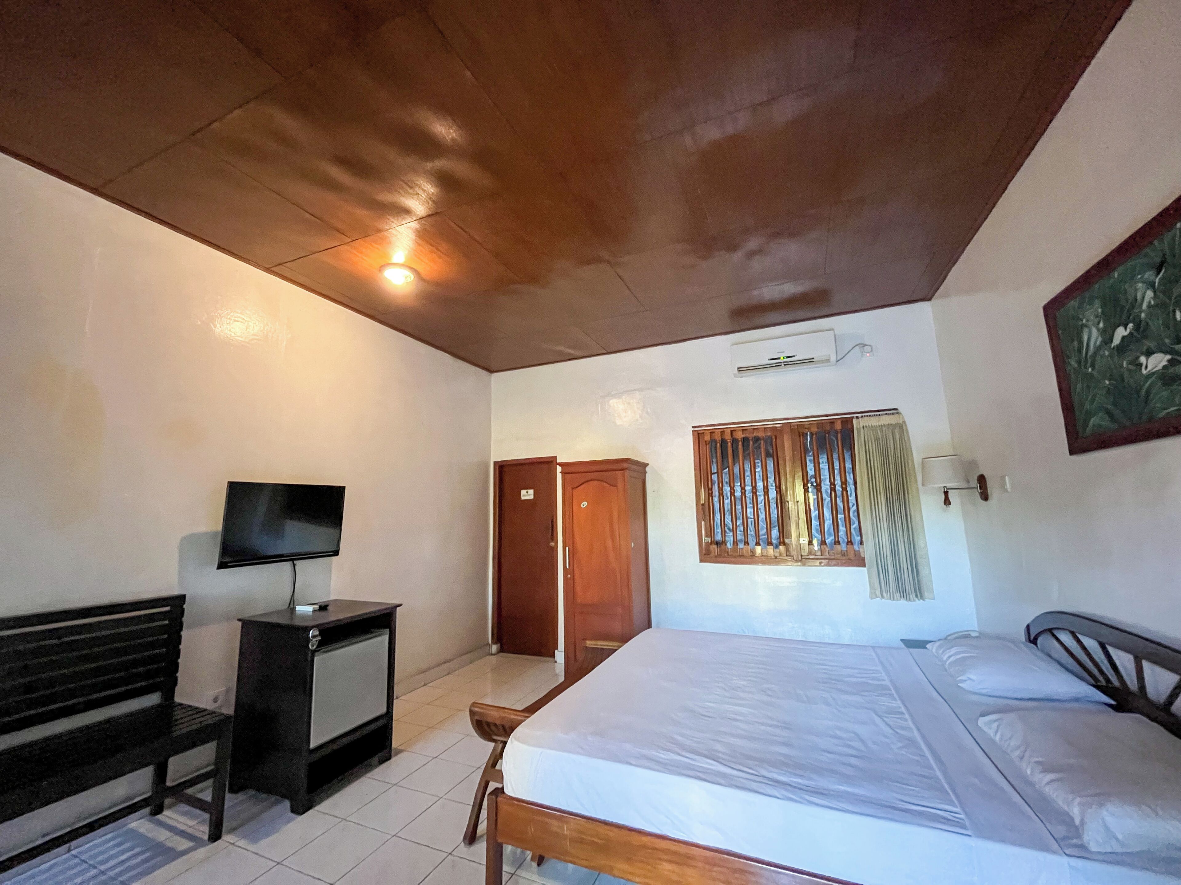 A bedroom with a bed, a TV on a small table, a wardrobe, and a window with blinds.