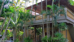 A two-story building with a balcony, surrounded by palm trees and greenery. - Suji Bungalow (Kuta)