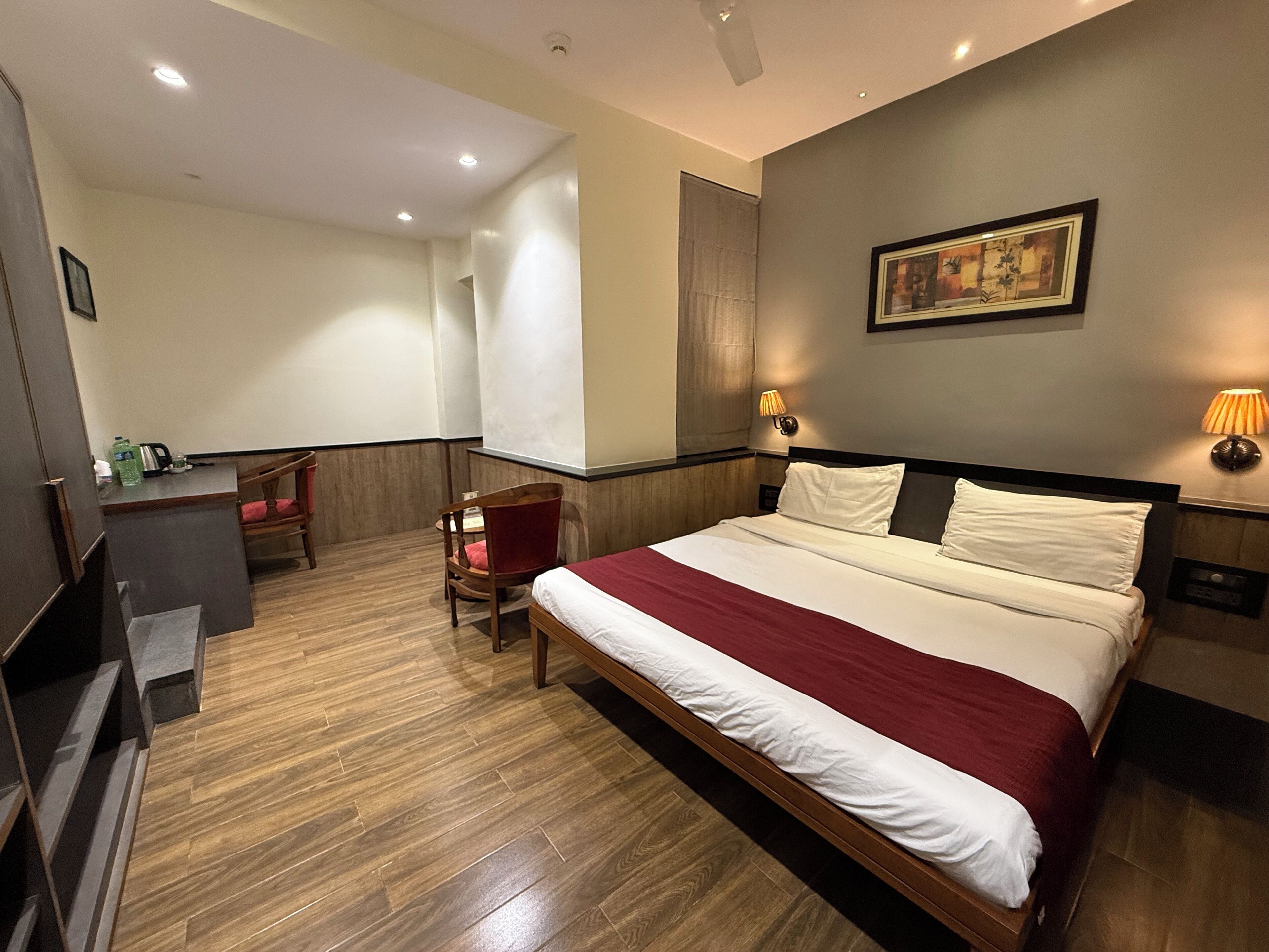 A hotel room with a large bed, a desk, a chair, and a painting on the wall.