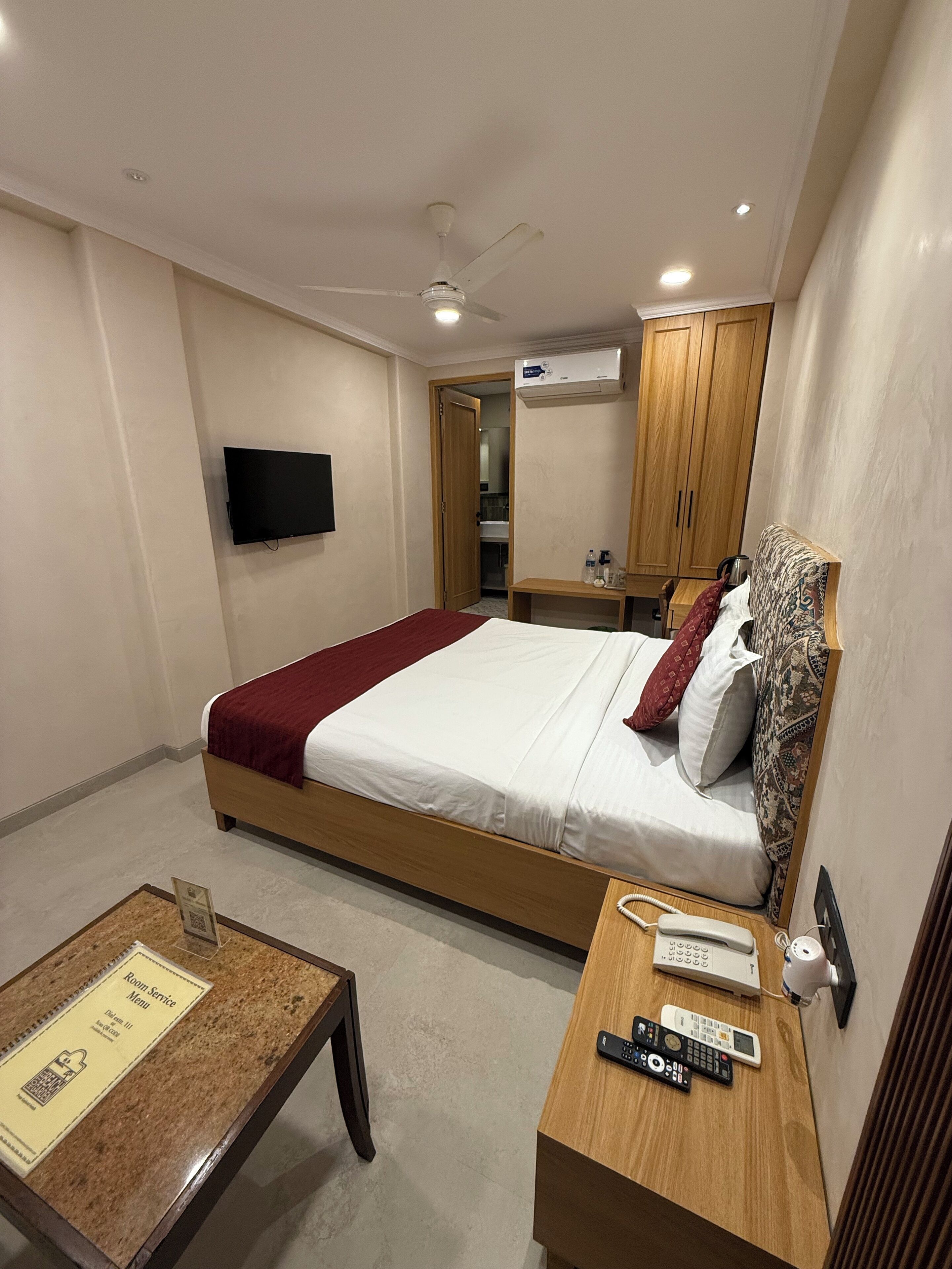 Ein Hotelzimmer mit Bett, Schreibtisch, Fernseher, Telefon und einem durch eine offene Tür einsehbaren Badezimmer.