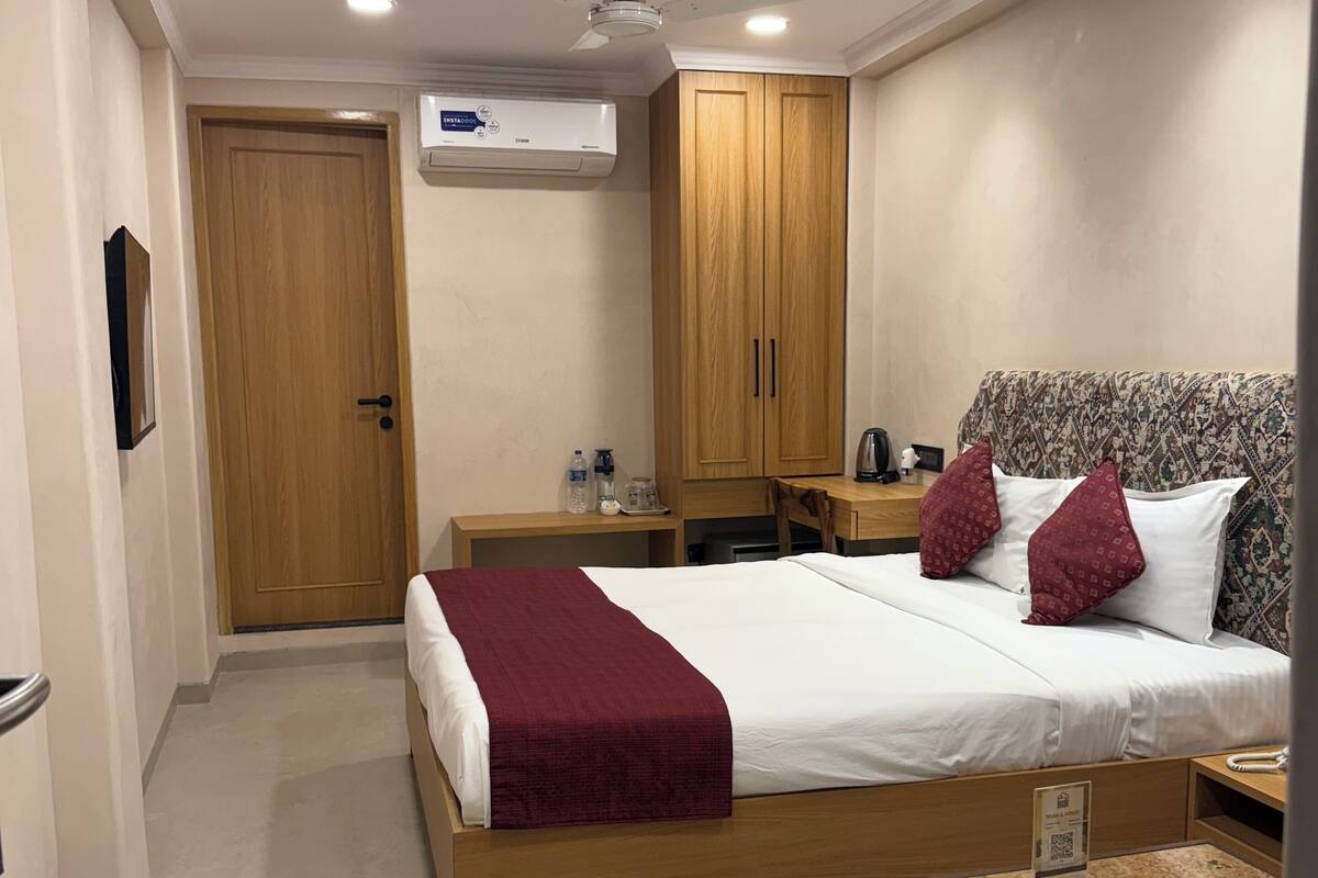 Ein Hotelzimmer mit Bett, Schreibtisch, Stuhl, Nachttisch, Kleiderschrank und Klimaanlage.