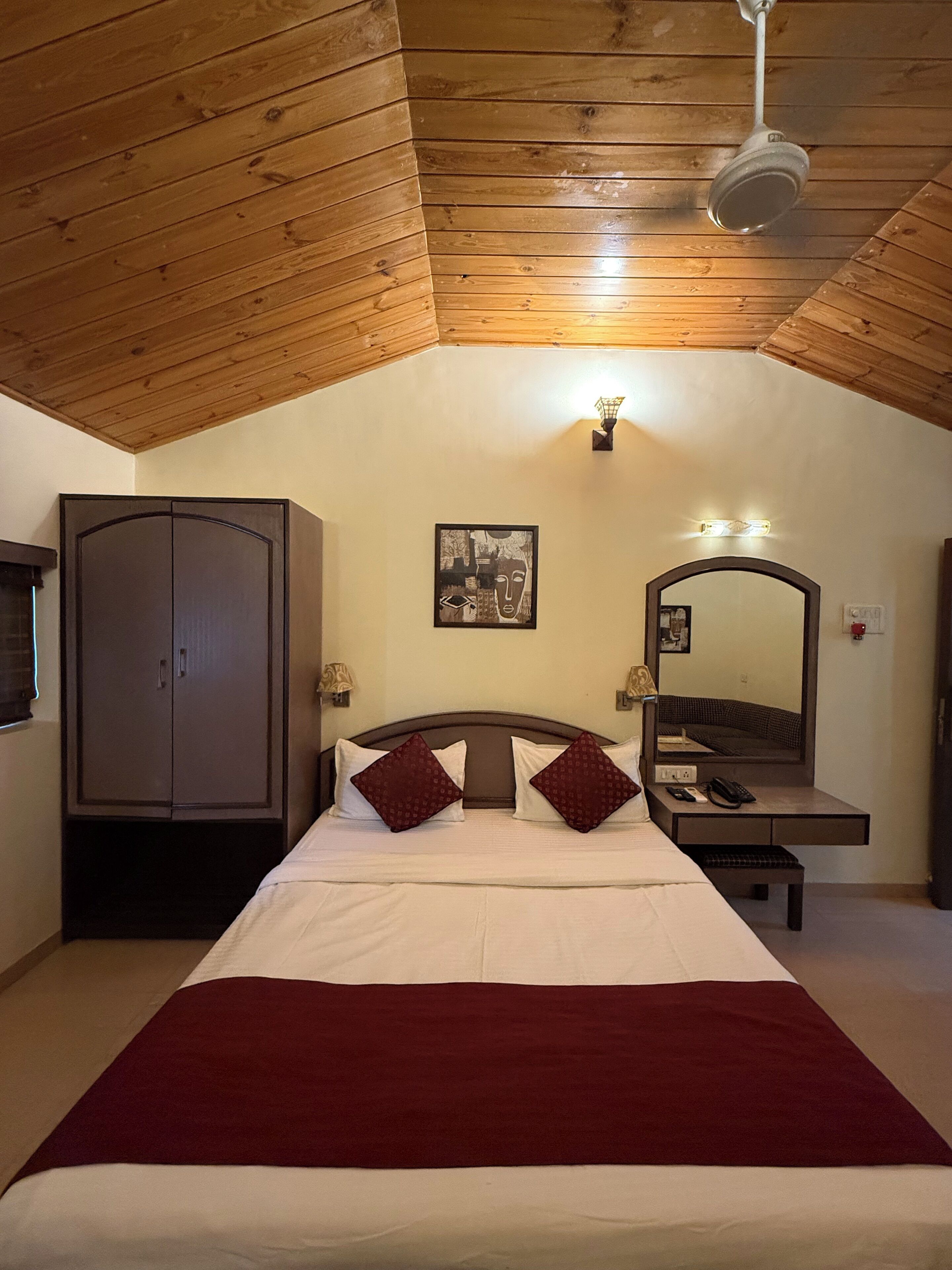 A bedroom with a bed, a wardrobe, a bedside table with a lamp, a mirror, and a ceiling fan.