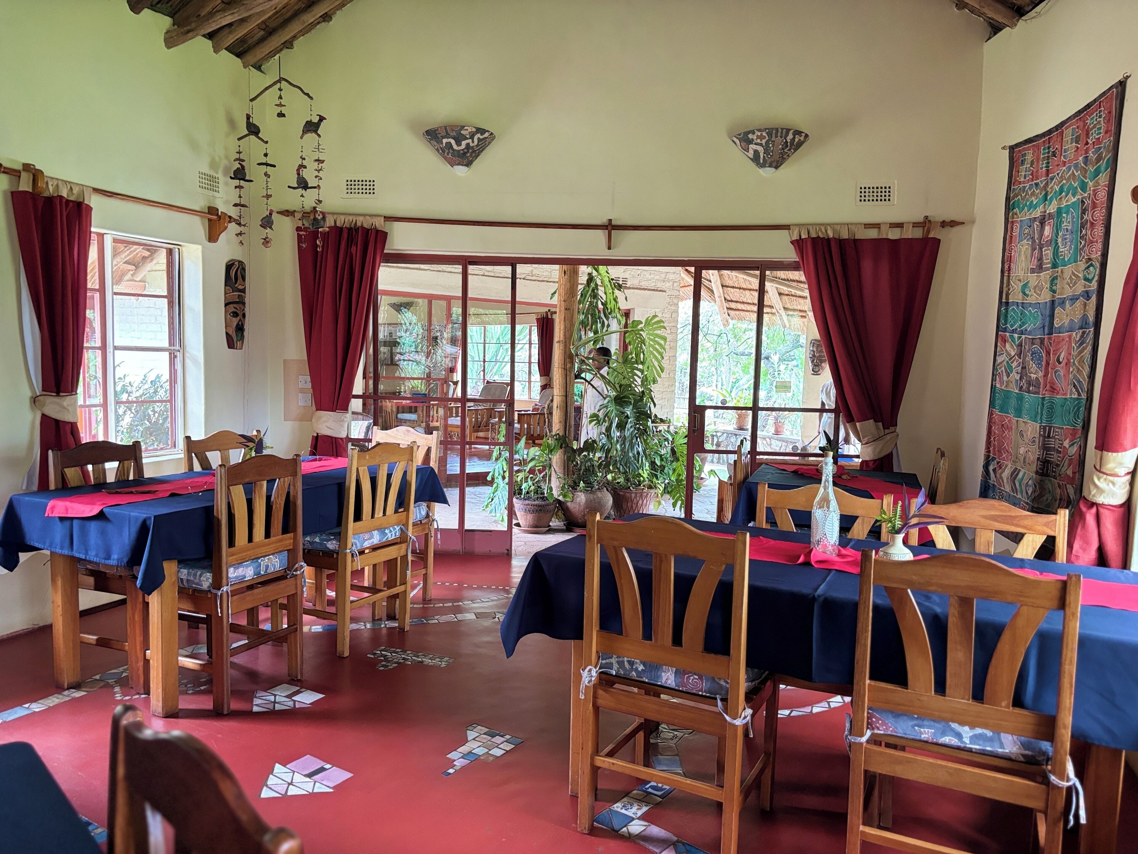 A dining area with wooden tables and chairs, red curtains, and a view of the outside.