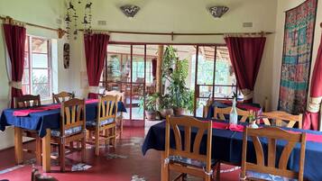 A dining area with wooden tables and chairs, red curtains, and a view of the outside.