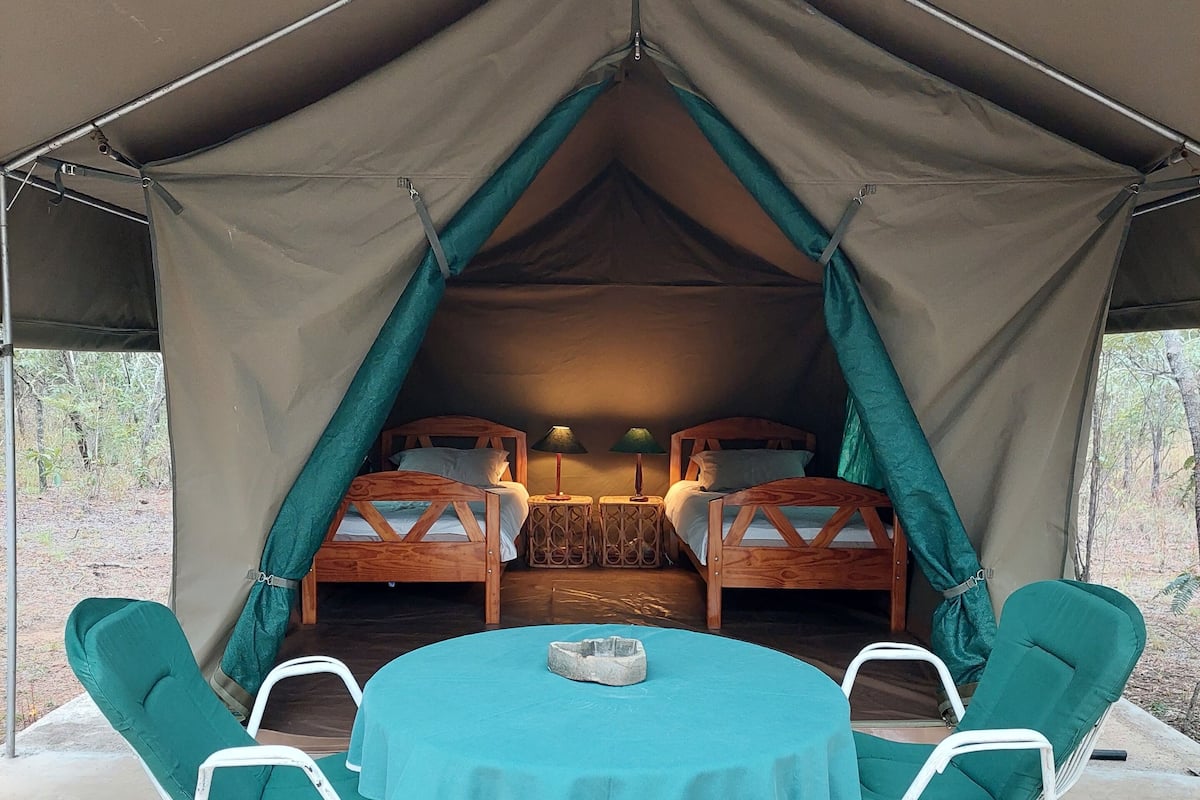A tented accommodation with two bunk beds, a round table with chairs, and a small stone fireplace.