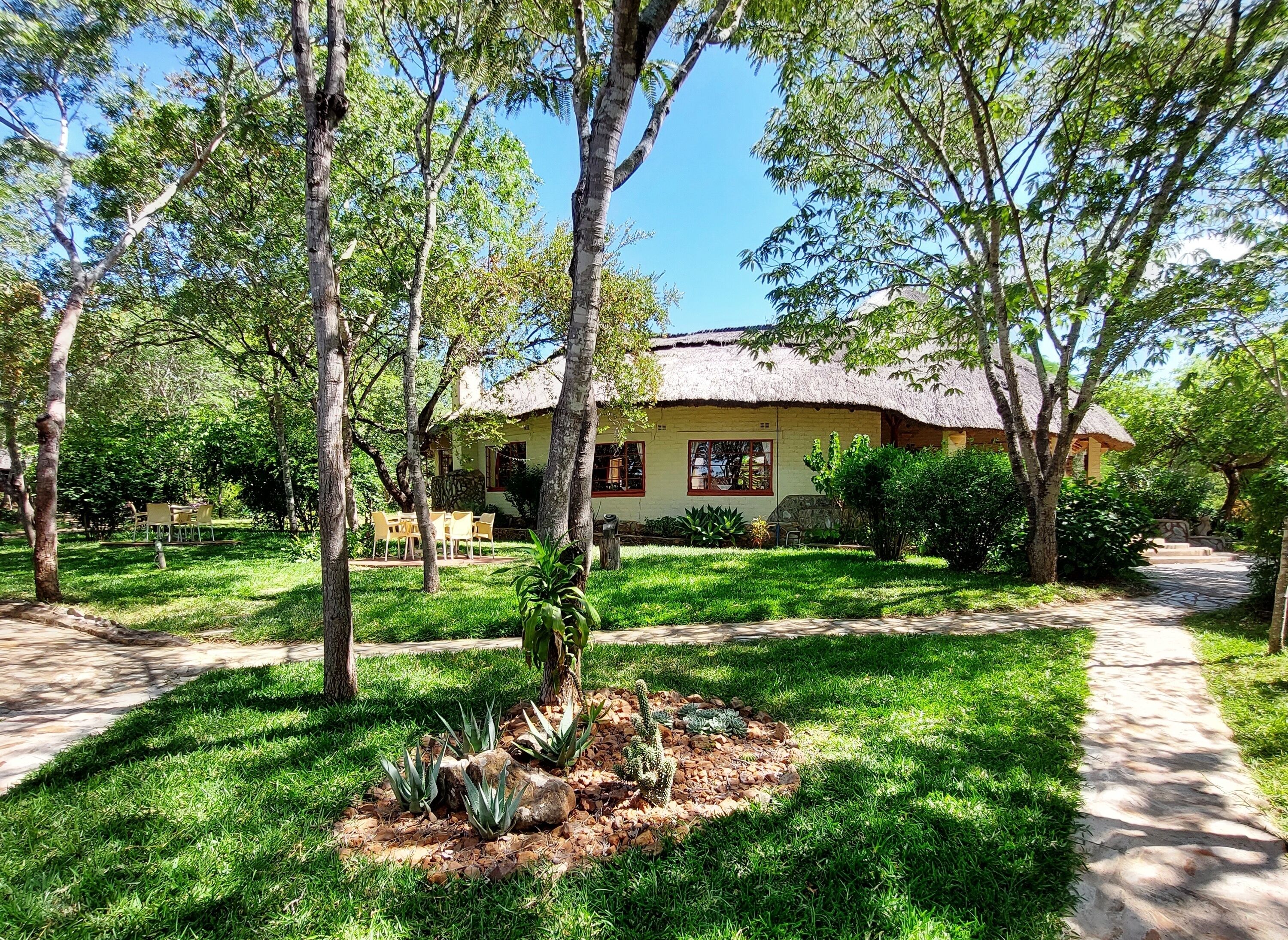 A house with a thatched roof, surrounded by a well-maintained garden with various plants and a patio area.