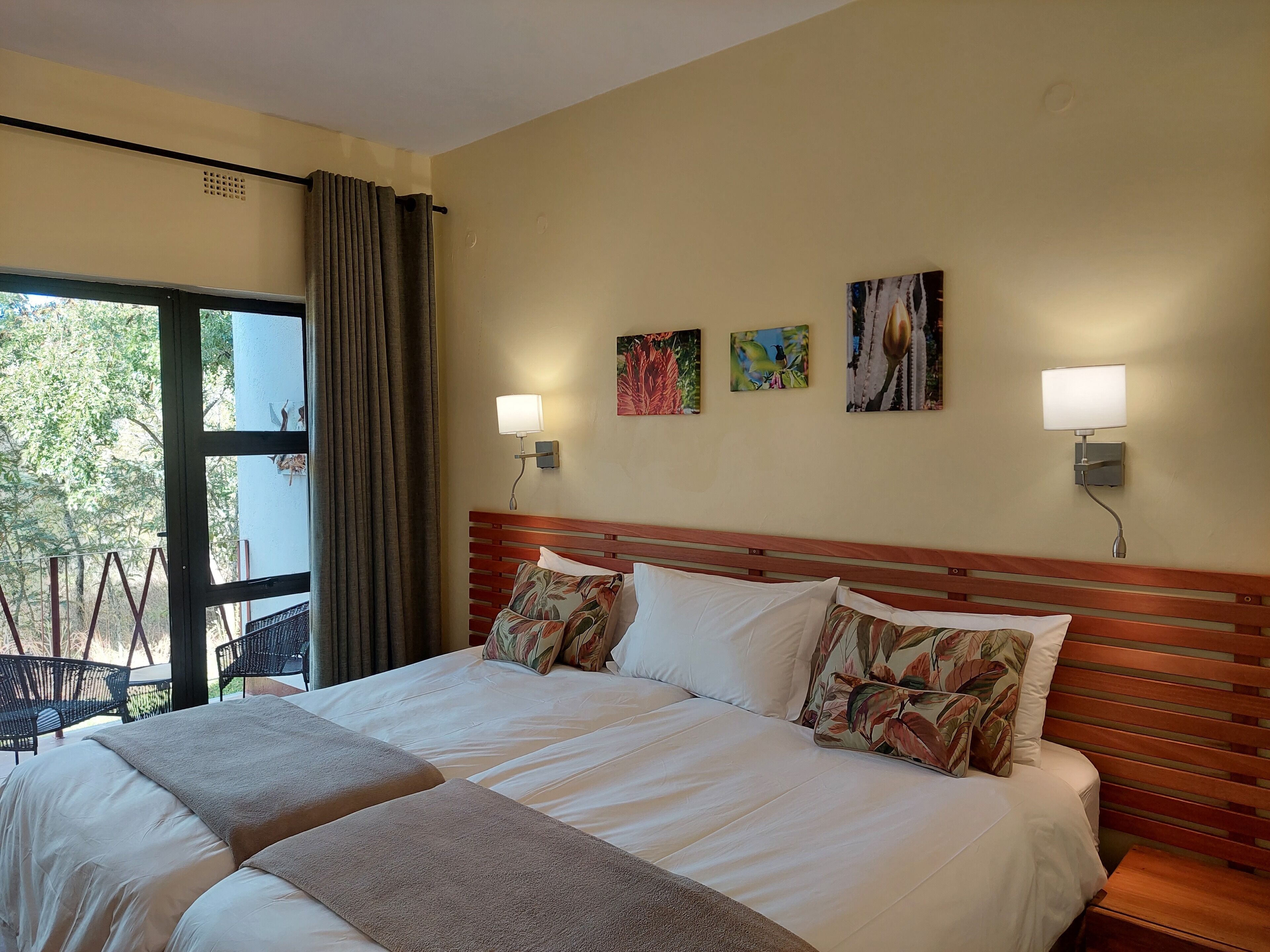 Una habitación de hotel con una cama grande, dos lámparas fijadas a la pared y tres cuadros enmarcados.