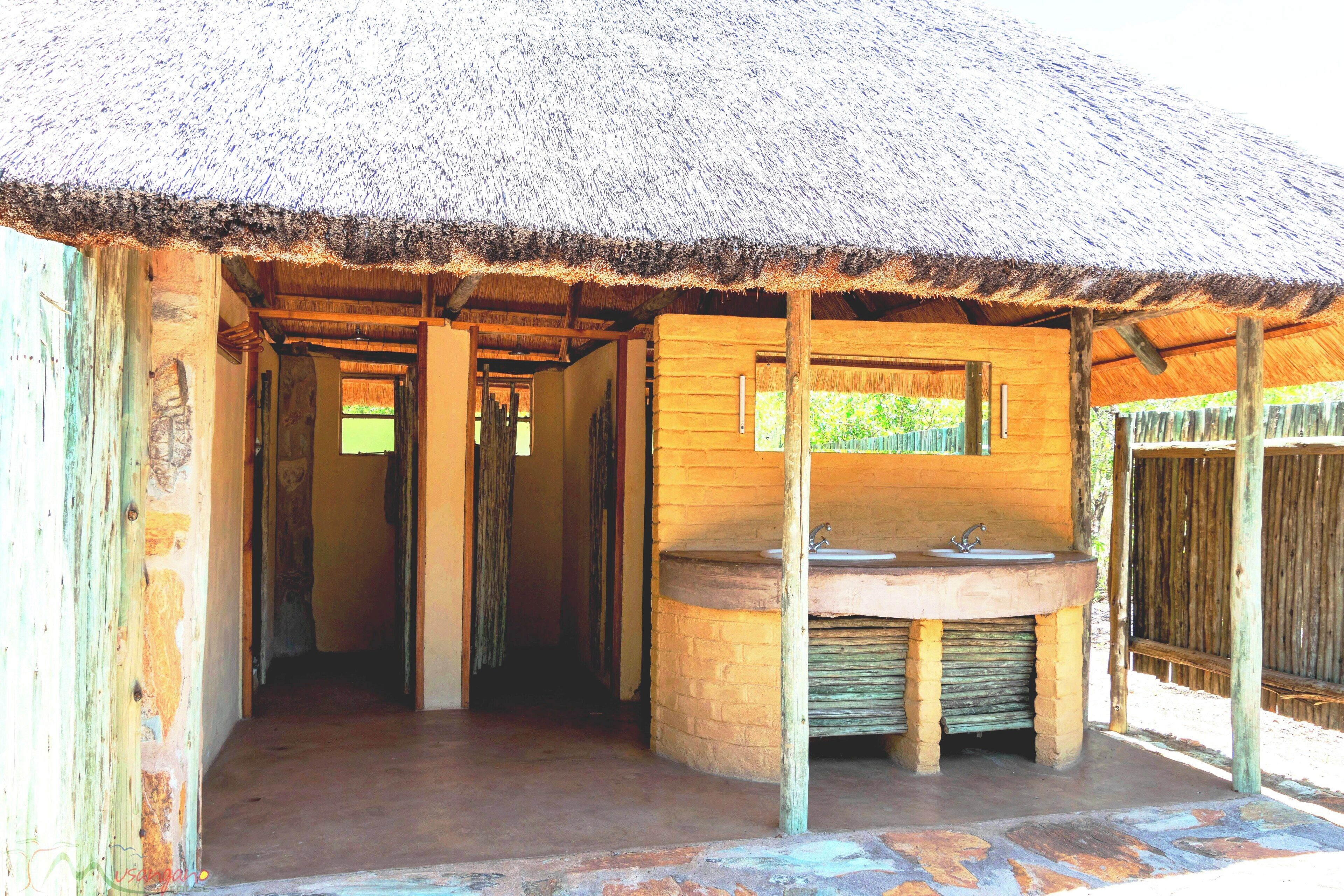 A rustic bathroom with a thatched roof, a stone sink, and wooden walls.