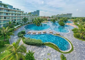 Un hotel con varias piscinas, palmeras y un diseño arquitectónico moderno.