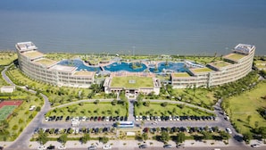 Un hotel gran amb una piscina central, diversos edificis amb sostres verds i vista al mar.