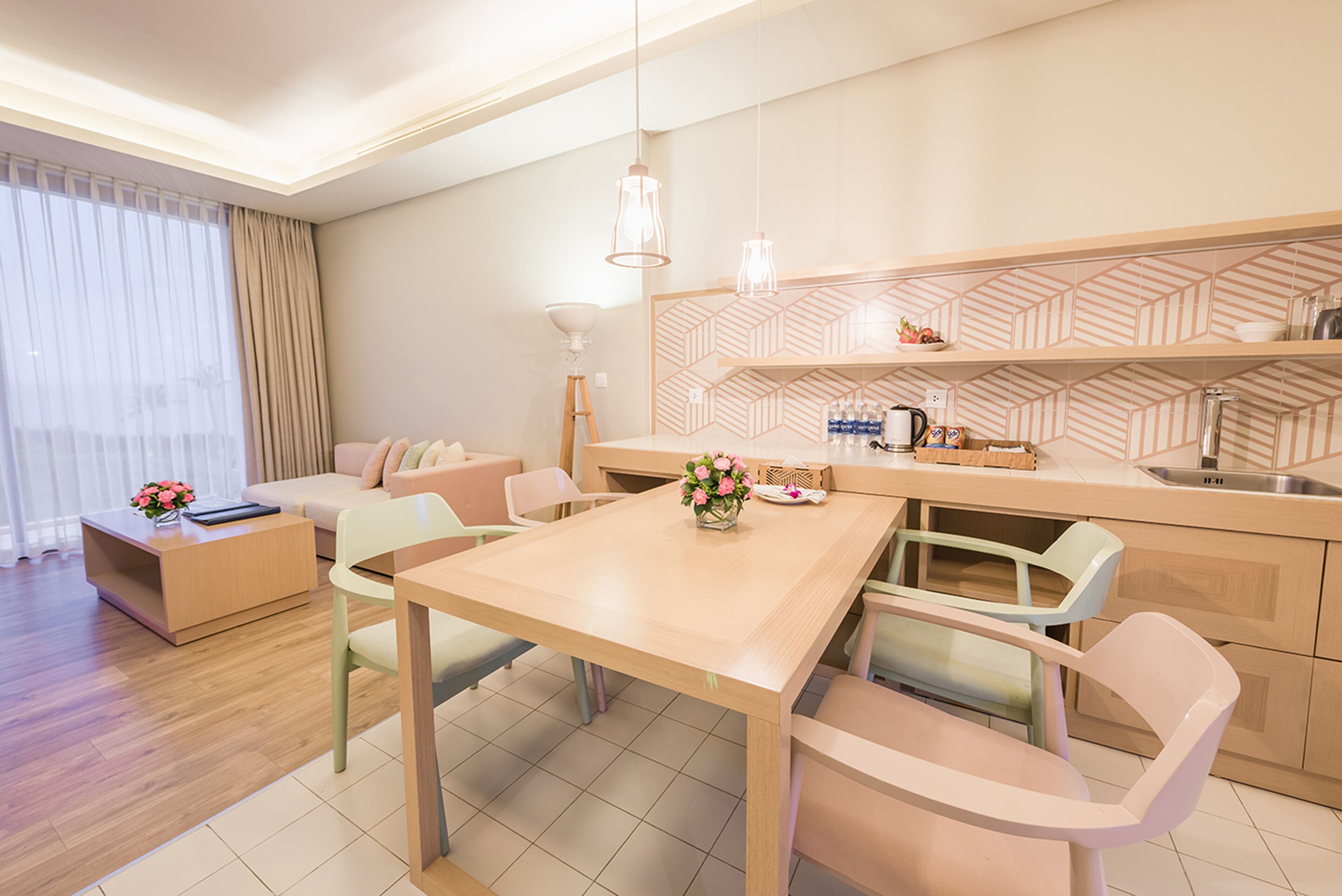 Ein modernes Wohnzimmer mit einem Holzesstisch, hellen Stühlen, einer Couch und einer Küchenzeile mit geometrischem Rücksprung.