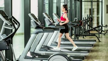 A woman walking on a treadmill in a gym with multiple treadmills and weight machines in the background.