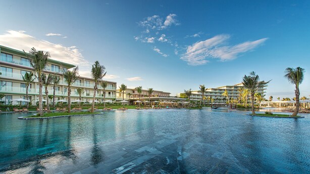 Un hotel amb una gran piscina d'infinity, palmeres i un cel blau clar.