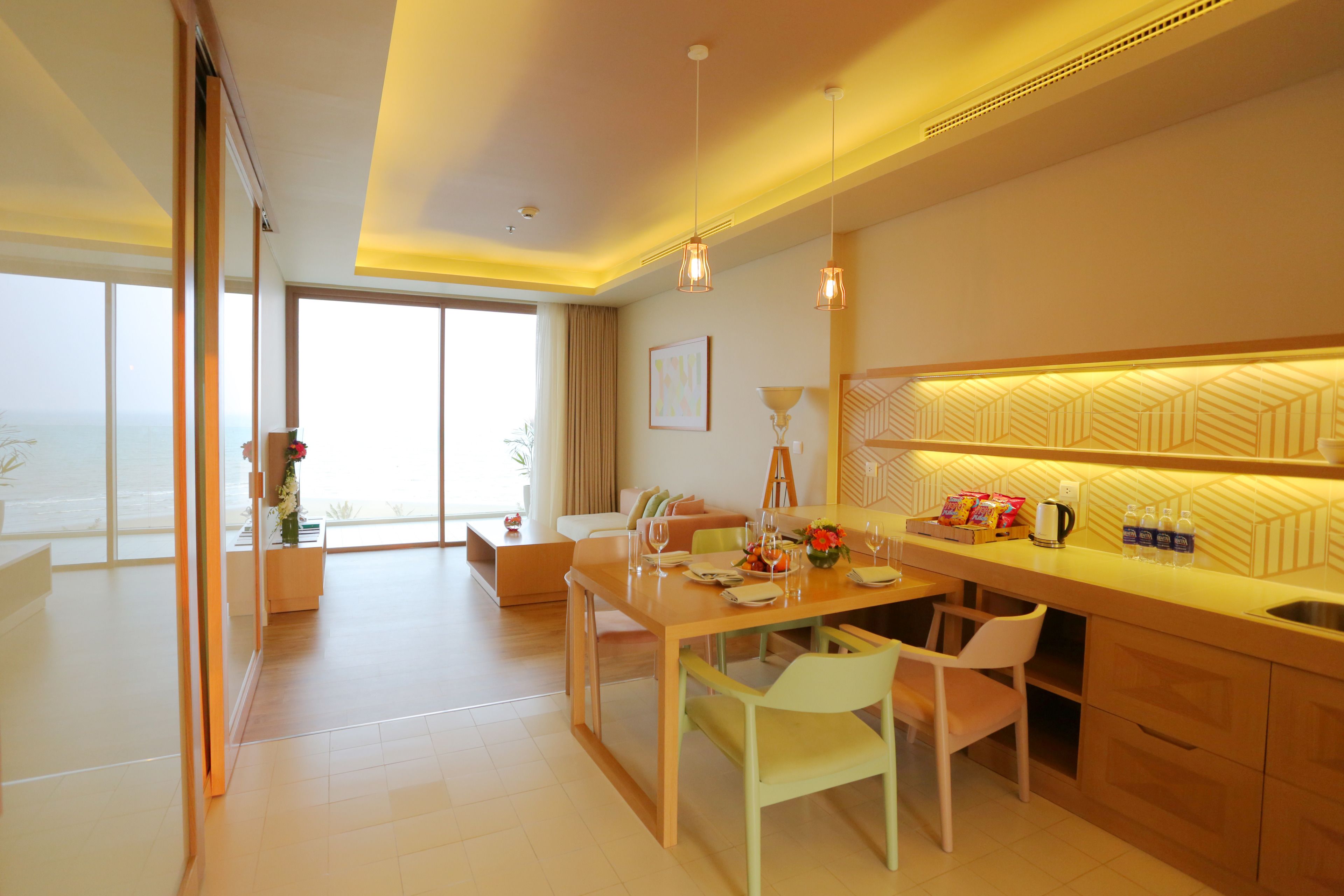 Una habitación de hotel moderna con comedor, cocina y grandes ventanales con vistas.