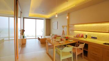 A modern hotel room with a dining area, a kitchen, and large windows offering a view.
