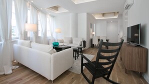 Un salón moderno con un sofá blanco, un sillón mecedor negro, un armario de madera y un televisor de pantalla plana.