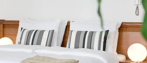 Una cama bien hecha con almohadas a rayas, un plaid color beige y lámparas de noche.