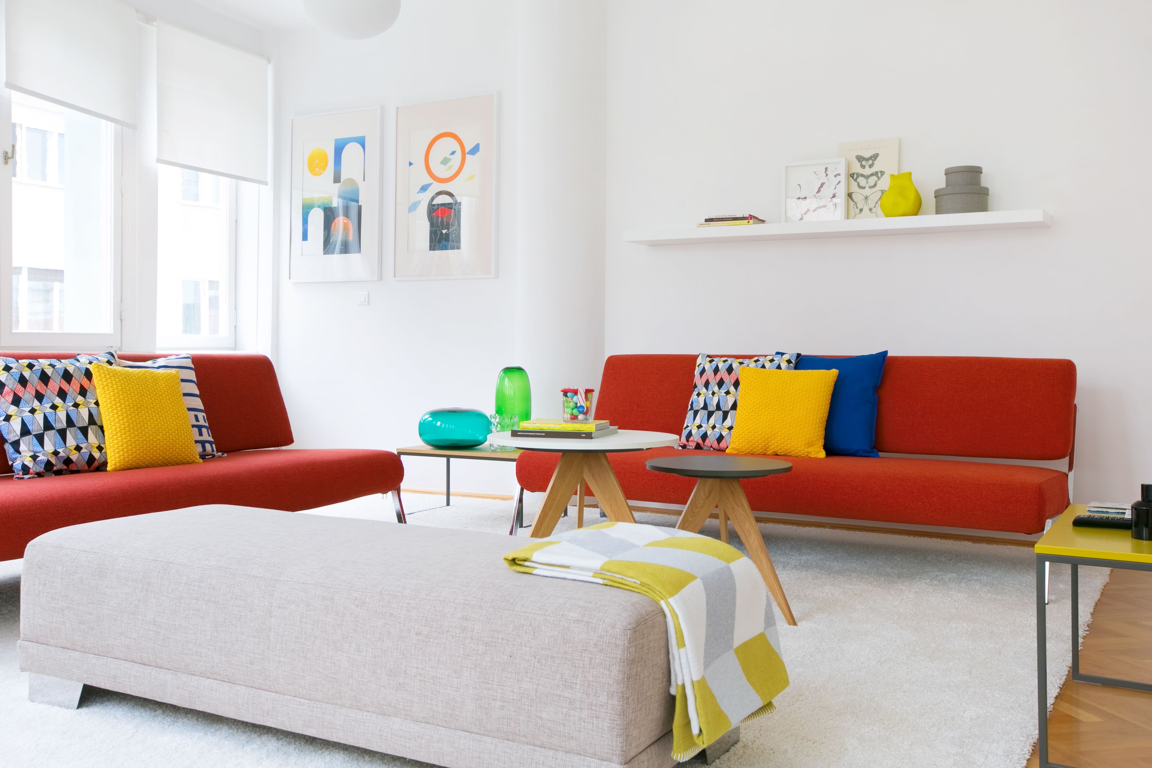 Una sala de estar moderna con un sofá rojo, un reposapiés beige y una pequeña mesa redonda con un jarrón verde y libros.