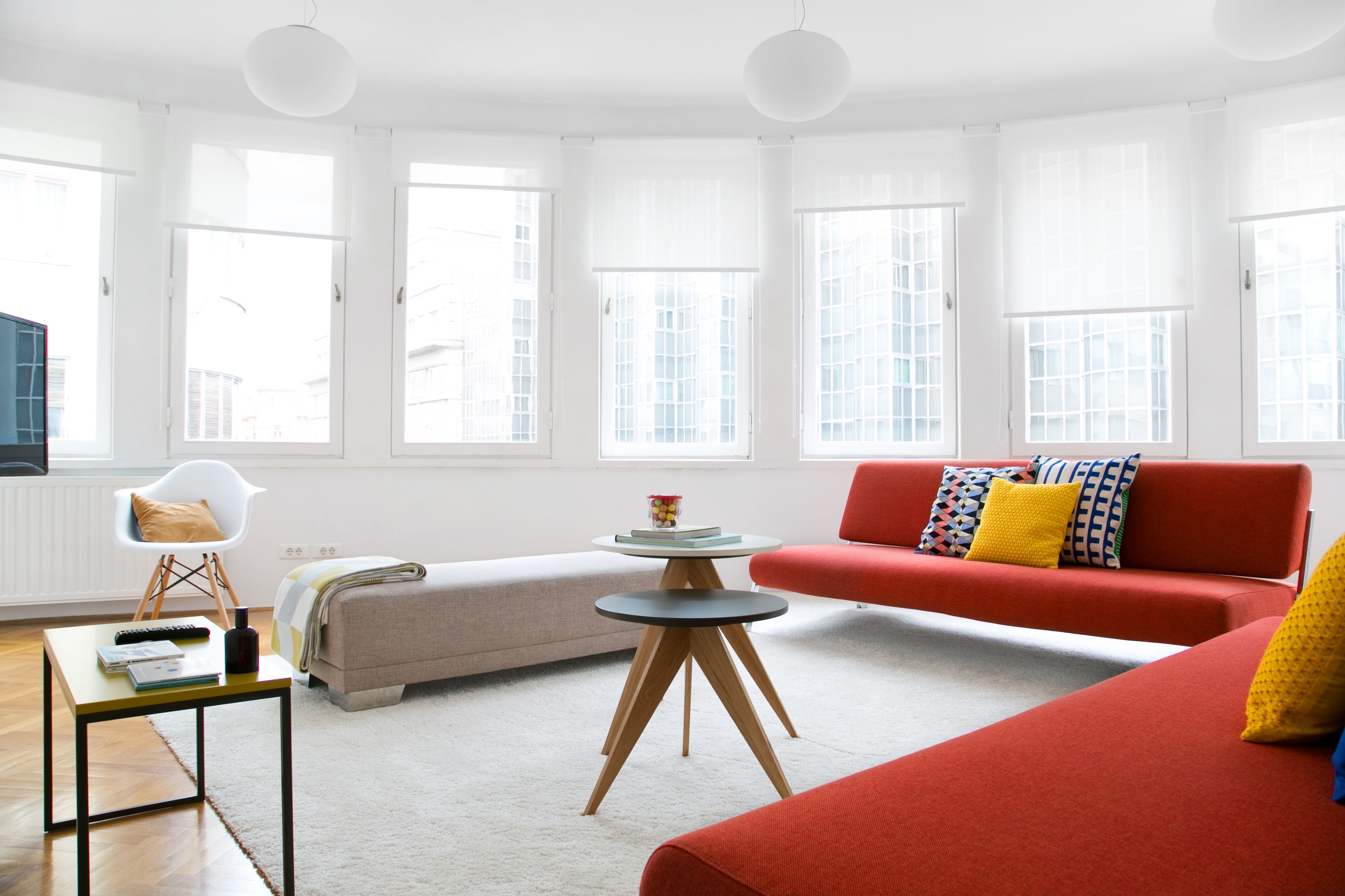 A modern living room with a red sofa, a white chair, a round coffee table, and a beige sofa.