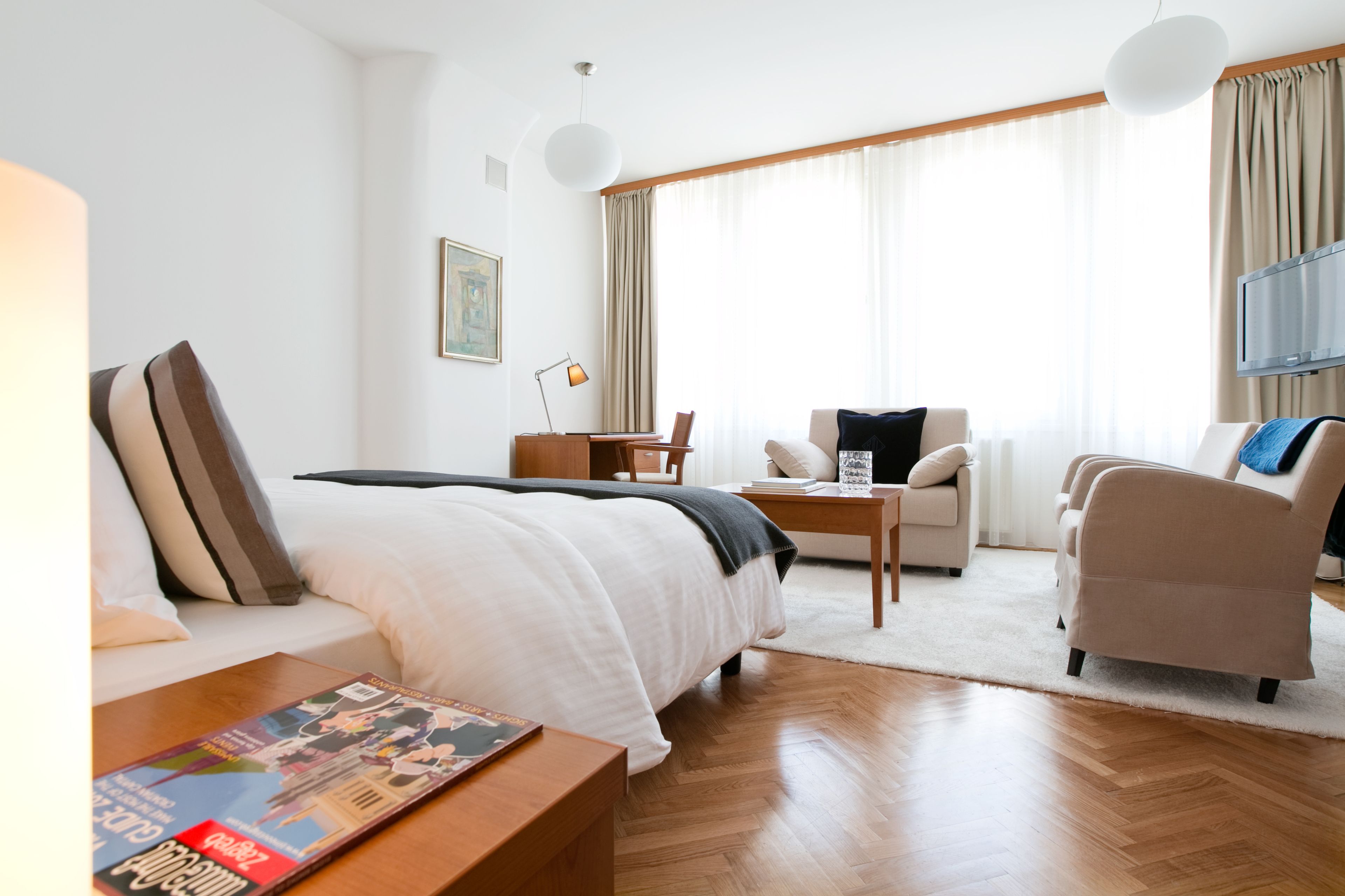 Ein Hotelzimmer mit einem Bett, zwei Sesseln, einem Sofa, einem Fernseher, einem Schreibtisch und einer Lampe.