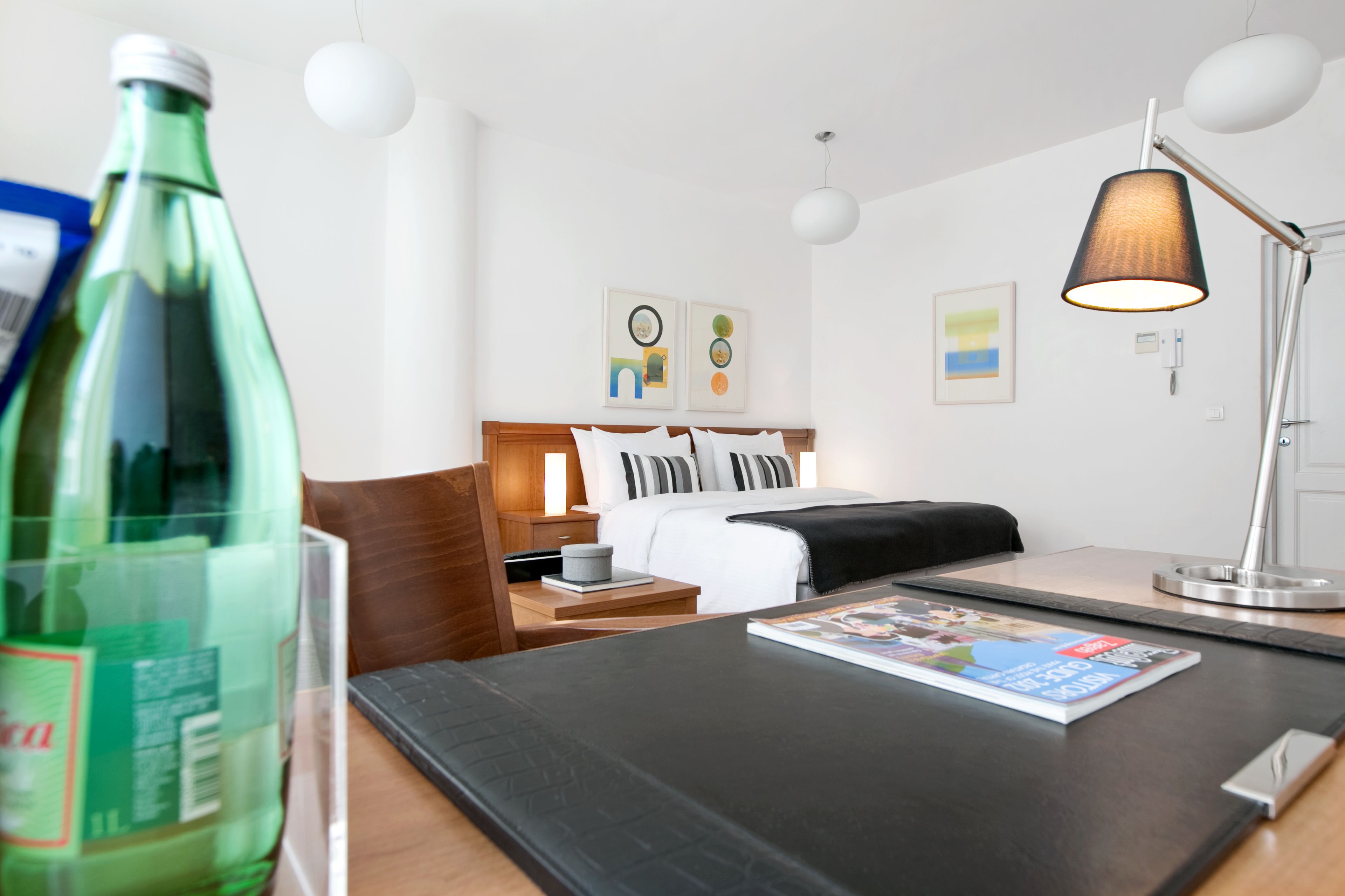 Una habitación de hotel con cama, mesita de noche, lámpara y una revista sobre la mesa.