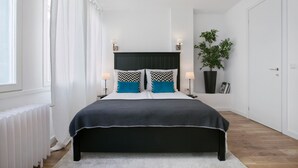 Un dormitorio moderno con una cama grande, cortinas blancas, una planta en maceta y un radiador.