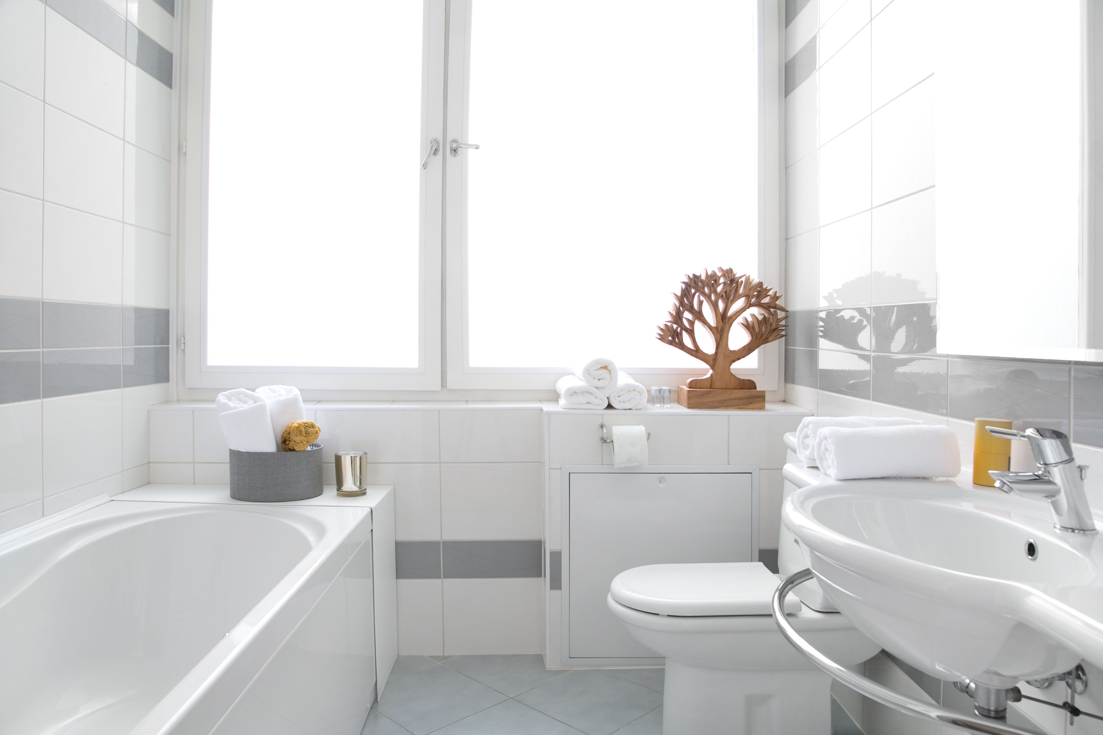 Een moderne badkamer met een badkuip, toilet en wastafel. Er is een raam met uitzicht op bomen, en handdoeken en toiletartikelen liggen op het aanrecht.